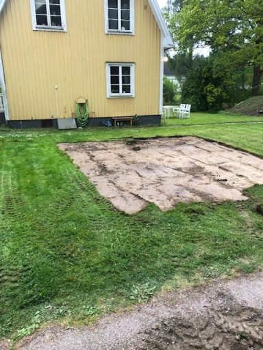 Gräsmatta med avbruten gräsyta vid ett gult hus och fönster.